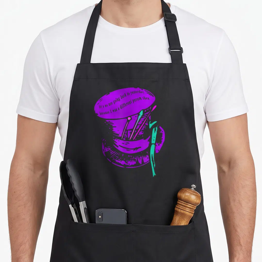 Mad hatter alice wonderland apron - Purple top hat with paintbrushes and artist quote in cartoon style — shown on a black cotton canvas apron against a white background