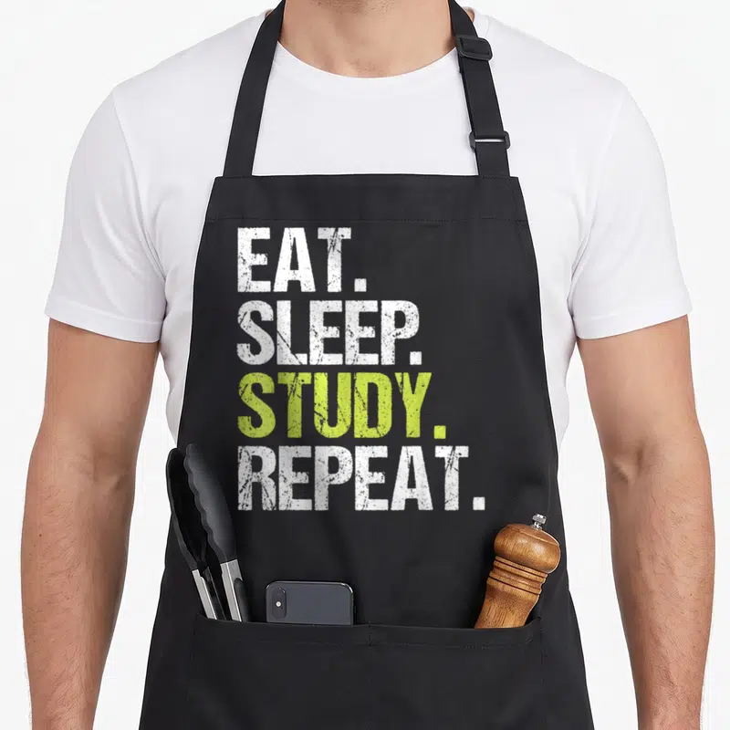 Sleep christmas apron - EAT SLEEP STUDY REPEAT text in white and lime green distressed font — shown on a black cotton canvas apron against a white background