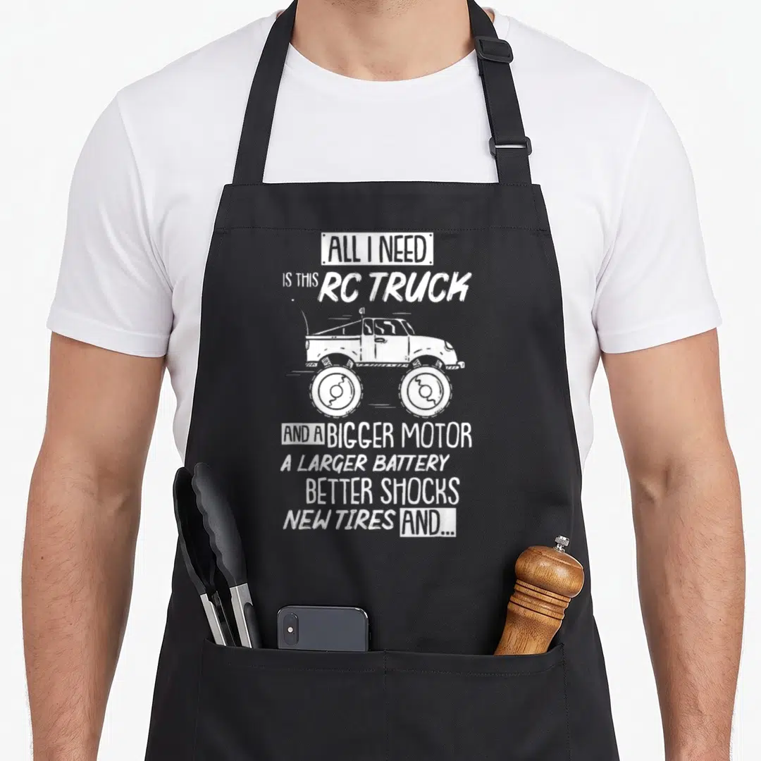Racing truck apron - White RC truck sketch with stacked text listing motor and tire upgrades — shown on a black cotton canvas apron against a white background