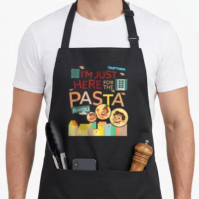 Luca pasta apron - Stacked text reading I'm just here for the pasta with cartoon faces and buildings below — shown on a black cotton canvas apron against a white background