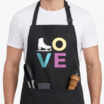 Ice figure skating apron - LOVE text with white skate replacing L, yellow O, blue V, pink E — shown on a black cotton canvas apron against a white background