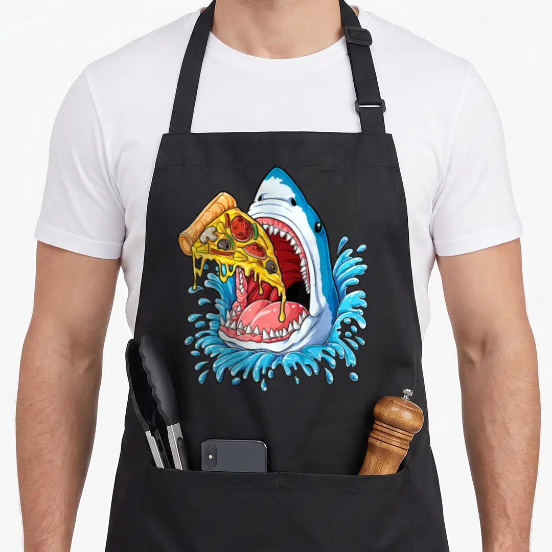 Eating pizza apron - Cartoon shark head in blue water grabbing a slice of pepperoni pizza with dripping cheese — shown on a black cotton canvas apron against a white background