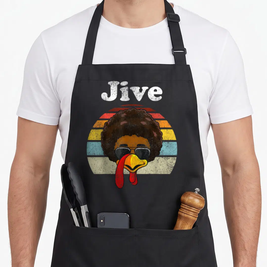 Jive thanksgiving day aprons - Cartoon turkey head with afro and sunglasses under Jive text over striped sun — shown on a black cotton canvas apron against a white background