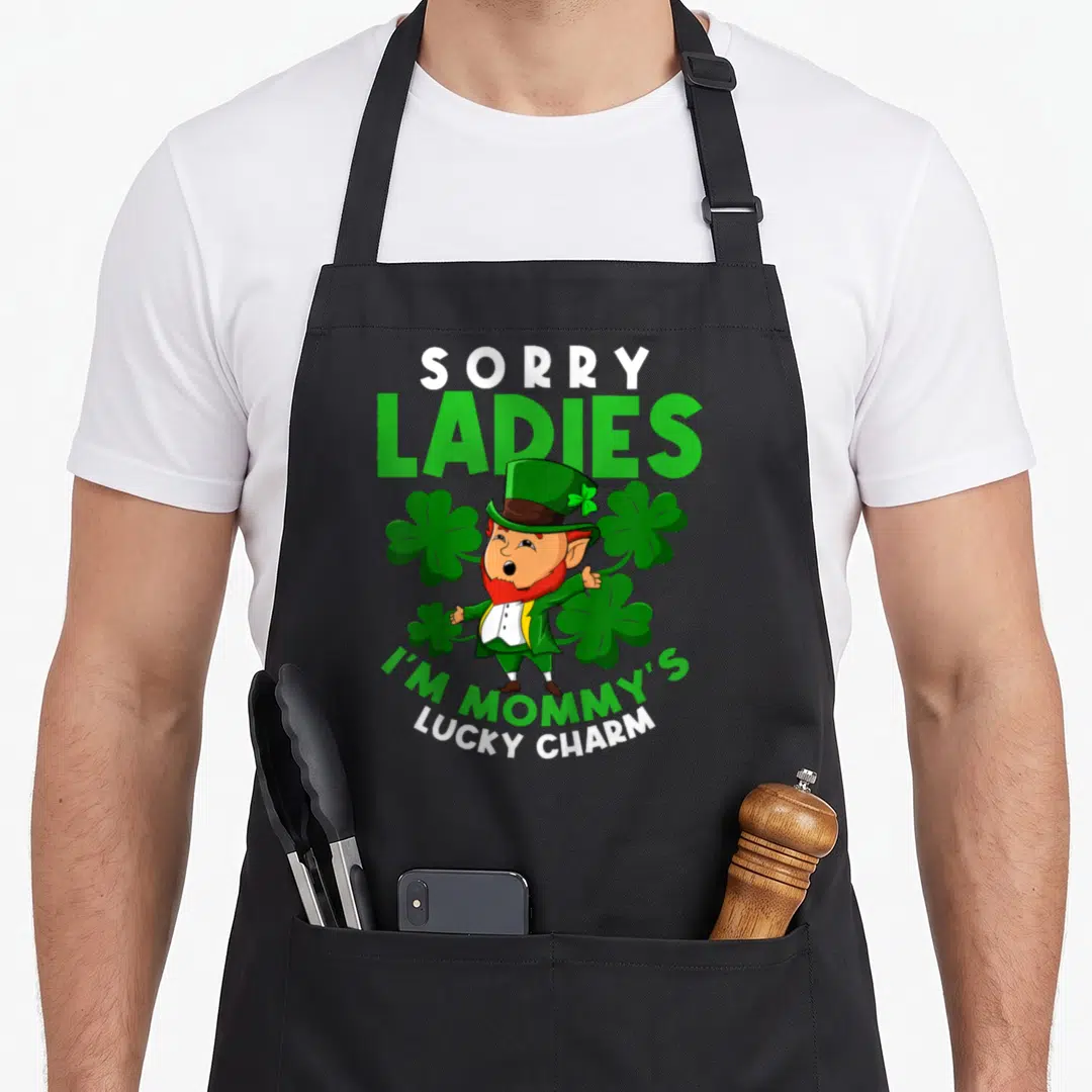 Charm leprechaun st patrick day aprons - Cartoon leprechaun with Sorry Ladies I'm Mommy's Lucky Charm text and shamrocks — shown on a black cotton canvas apron against a white background