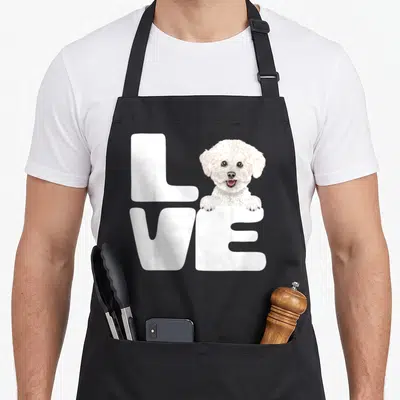 Frise dog apron - White cartoon dog replacing O in two-row LOVE text with paws on bottom letter — shown on a black cotton canvas apron against a white background