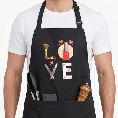 Technician tech manicurist apron - Makeup tools arranged to spell LOVE in red, pink, brown, and white cartoon art — shown on a black cotton canvas apron against a white background