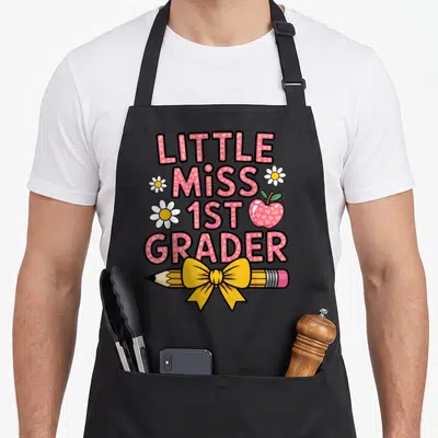 1st grader miss grade apron - Pink text LITTLE MISS 1ST GRADER with yellow pencil bow and white daisies — shown on a black cotton canvas apron against a white background