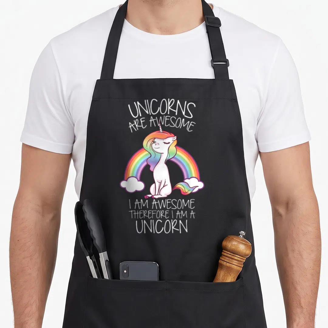 Therefore unicorn apron - Cartoon white unicorn sitting in front of rainbow with purple outline and clouds — shown on a black cotton canvas apron against a white background