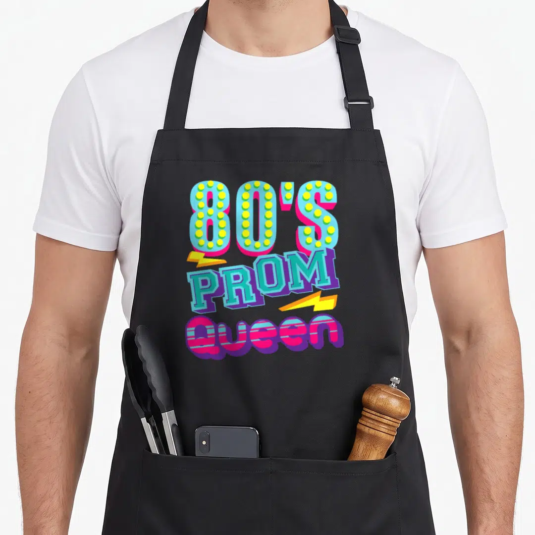 Throwback queen apron - Stacked 80s Prom Queen text with yellow lightning bolts in blue pink yellow and purple — shown on a black cotton canvas apron against a white background