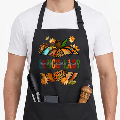Pumpkin lunch lady apron - Leopard print pumpkins with LUNCH LADY text and thankful grateful blessed script surrounded — shown on a black cotton canvas apron against a white background
