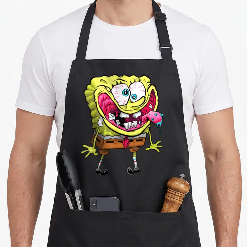 Wired general apron - Zombie sponge character with bloodshot eyes, jagged teeth, and detached tongue in cartoon style — shown on a black cotton canvas apron against a white background