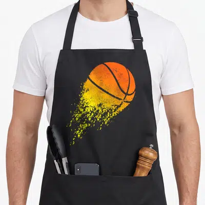 Basketball sports fan apron - Orange basketball with yellow splattered tail and distressed texture on grey background — shown on a black cotton canvas apron against a white background
