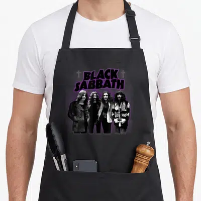 Sabbath cross apron - Purple BLACK SABBATH text with two crosses above a black and white photo of four men — shown on a black cotton canvas apron against a white background