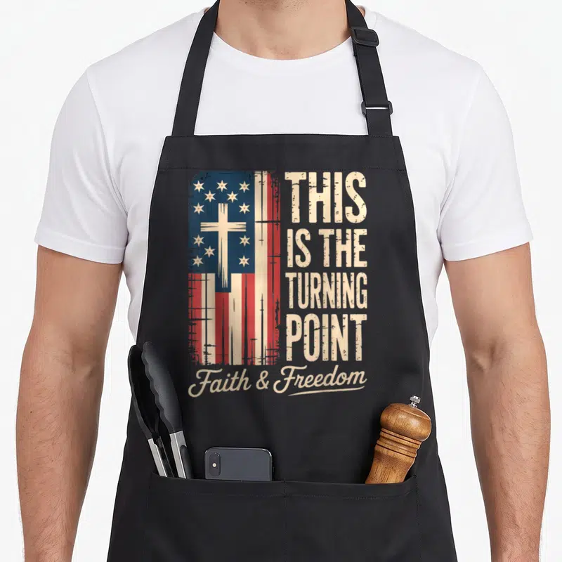 Turning patriotic apron - Distressed flag with cross, stacked text THIS IS THE TURNING POINT, script Faith & Freedom — shown on a black cotton canvas apron against a white background