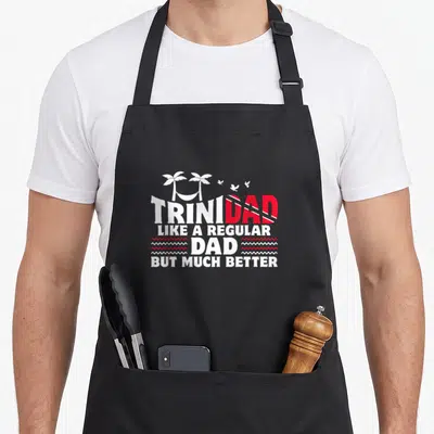 Trini country apron - Retro text design with palm trees, hammock, birds, and Trinidad and Tobago flag colors — shown on a black cotton canvas apron against a white background