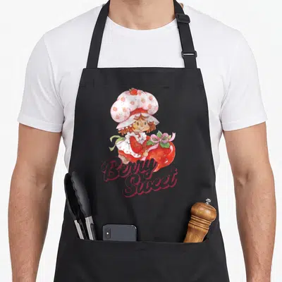 Berry strawberry apron - Cartoon girl in pink hat holds red strawberry above stacked Berry Sweet script text — shown on a black cotton canvas apron against a white background