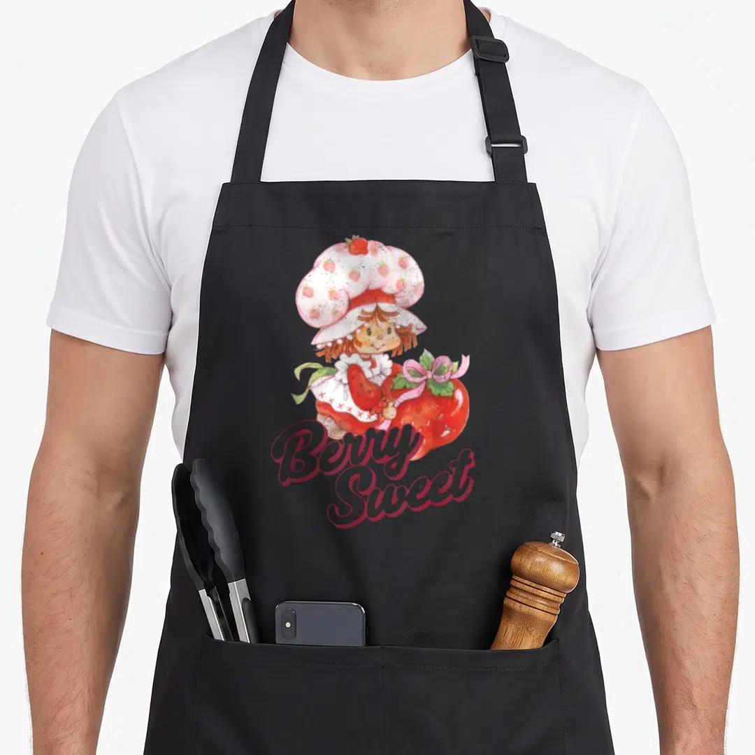 Berry strawberry apron - Cartoon girl in pink hat holds red strawberry above stacked Berry Sweet script text — shown on a black cotton canvas apron against a white background