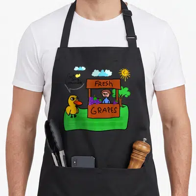 Fresh duck apron - Cartoon duck next to brown stand selling purple grapes with text Got any Lemonade — shown on a black cotton canvas apron against a white background