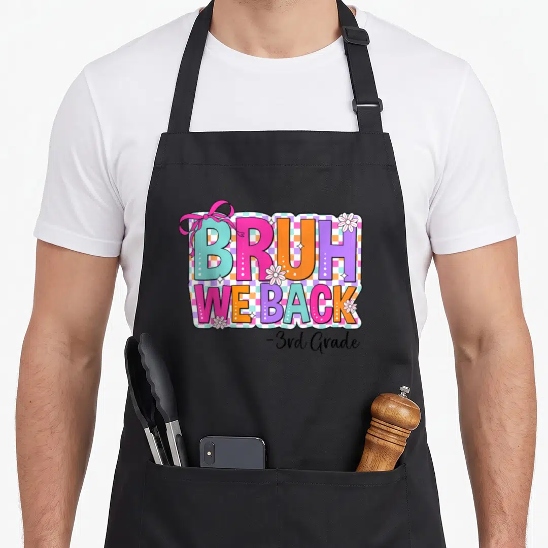 Grade bow apron - Colorful BRUH WE BACK text with pink bow and white flowers on checkered background — shown on a black cotton canvas apron against a white background