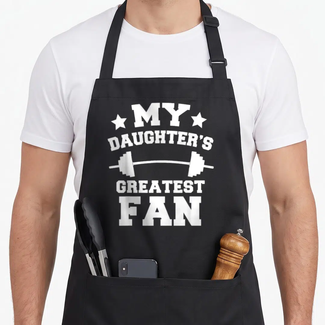 Powerlifting mom daughter apron - White stacked text MY DAUGHTER'S GREATEST FAN with barbell and stars — shown on a black cotton canvas apron against a white background