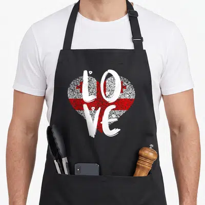 Georgian pride apron - Red and white heart containing Georgian flag pattern with vertical white LOVE script text — shown on a black cotton canvas apron against a white background