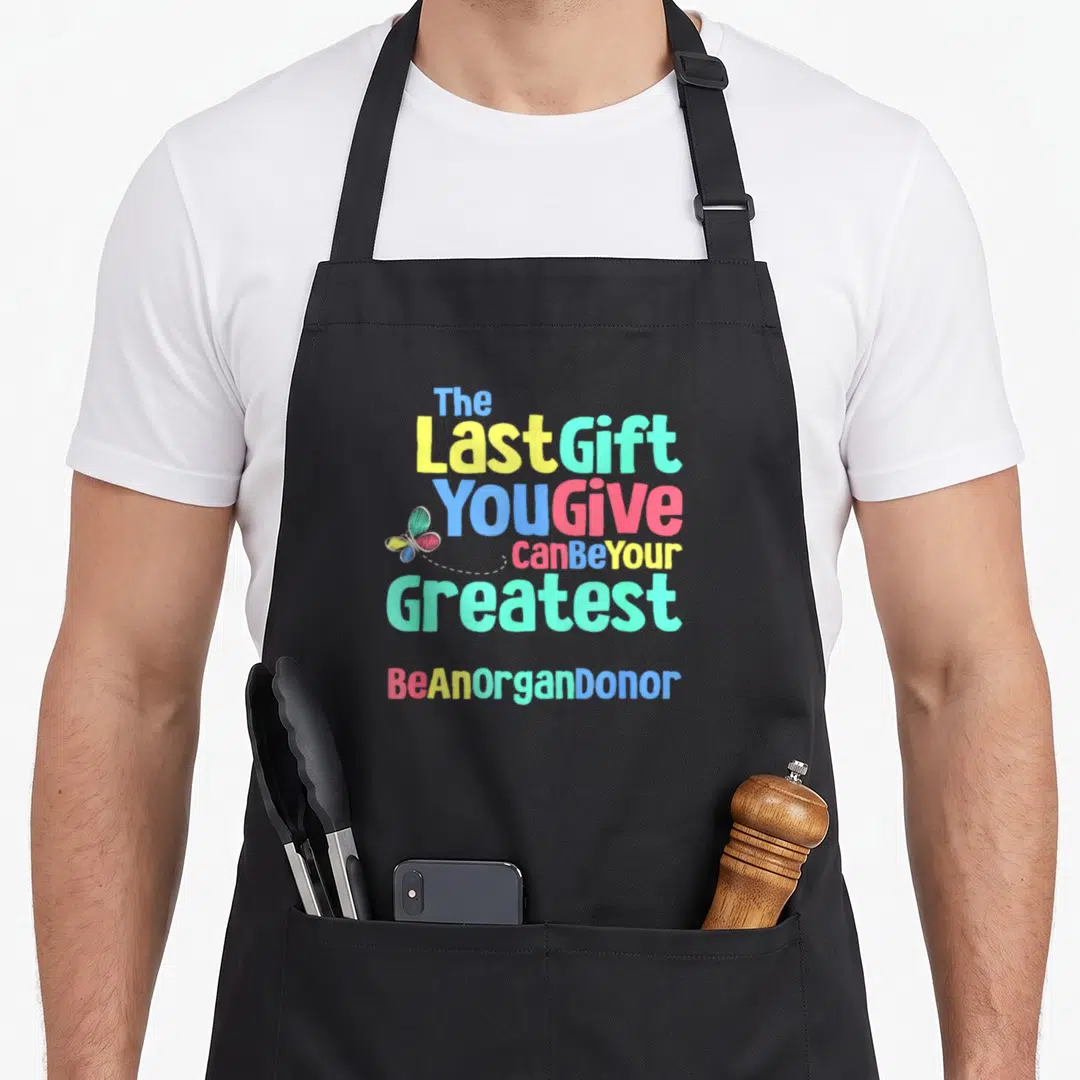 Donor donation organ apron - Stacked colorful text reading The Last Gift You Give Can Be Your Greatest — shown on a black cotton canvas apron against a white background