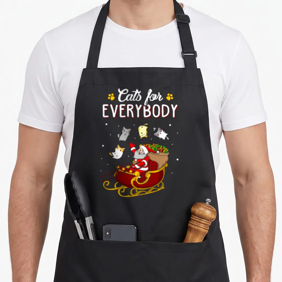 Everybody ugly christmas apron - Santa sleigh with floating cats and paw prints under Cats for Everybody text — shown on a black cotton canvas apron against a white background