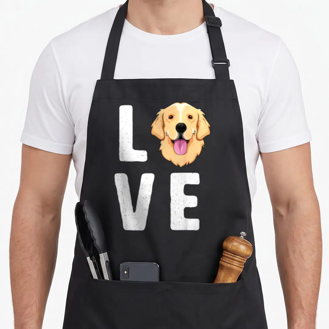 Dog pet golden retriever apron - Cartoon golden retriever head replaces O in white LOVE text with pink tongue — shown on a black cotton canvas apron against a white background