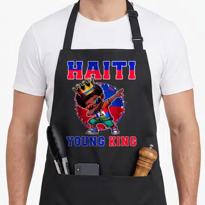 Young king apron - Cartoon boy dabbing with HAITI YOUNG KING text and flag colors — shown on a black cotton canvas apron against a white background