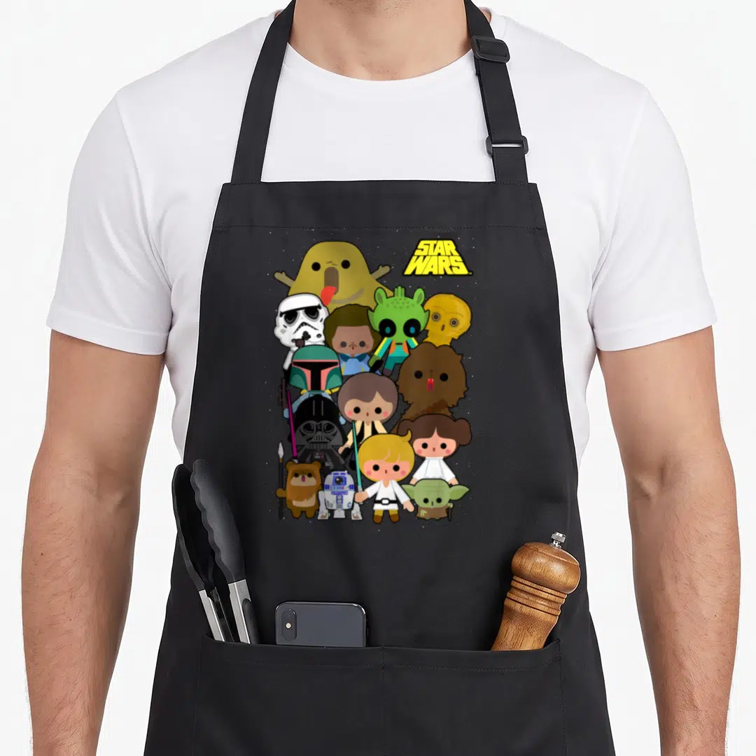 Shot kawaii apron - Chibi Star Wars characters stacked vertically with logo in yellow brown green and white — shown on a black cotton canvas apron against a white background