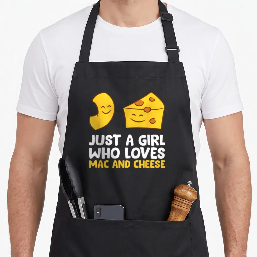 Vintage cheese mac apron - Cartoon macaroni and cheese wedge with faces above JUST A GIRL WHO LOVES MAC AND CHEESE text — shown on a black cotton canvas apron against a white background