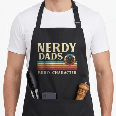 Nerdy grill daddy apron - Retro d20 die over beige teal orange maroon stripes with NERDY DADS BUILD CHARACTER text — shown on a black cotton canvas apron against a white background