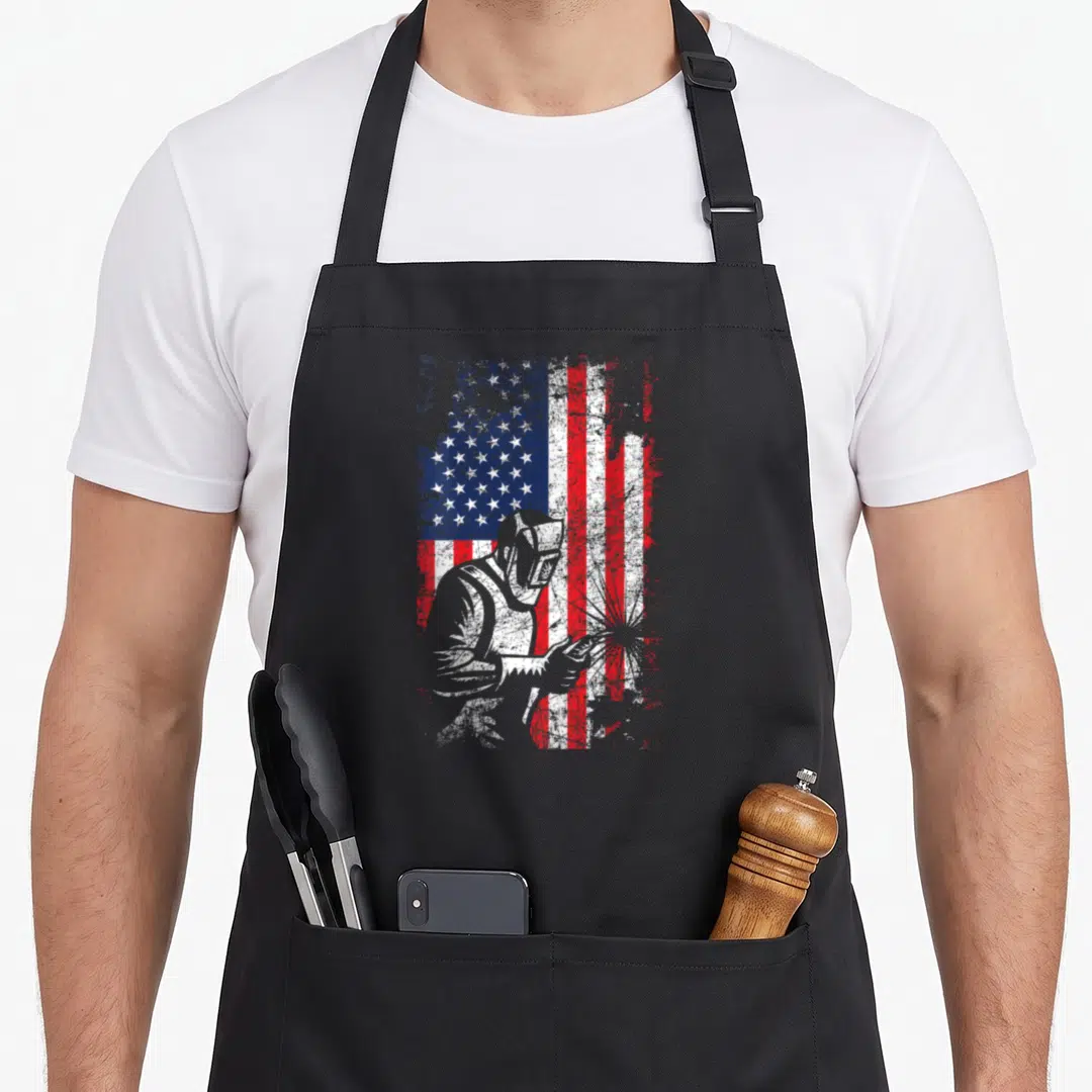Welding father day apron - Distressed USA flag with white welder silhouette and flying sparks on right side — shown on a black cotton canvas apron against a white background
