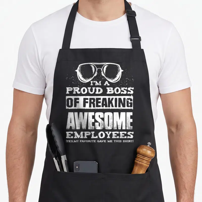 Freaking boss apron - White glasses above stacked text I'M A PROUD BOSS OF FREAKING AWESOME EMPLOYEES with distressed — shown on a black cotton canvas apron against a white background