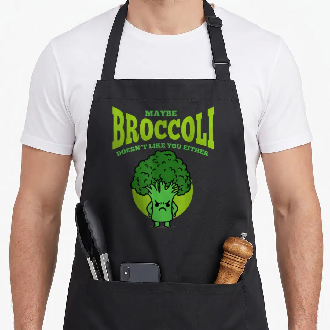 Maybe vegan apron - Angry cartoon broccoli character with green and lime text reading Maybe Broccoli Doesn't Like You — shown on a black cotton canvas apron against a white background