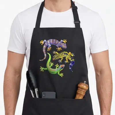 Wildlife gecko apron - Three realistic geckos in blue, yellow, green, and orange spotted patterns — shown on a black cotton canvas apron against a white background