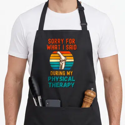 Surgery my therapy apron - Retro knee joint over striped sun with text sorry for what I said during physical therapy — shown on a black cotton canvas apron against a white background