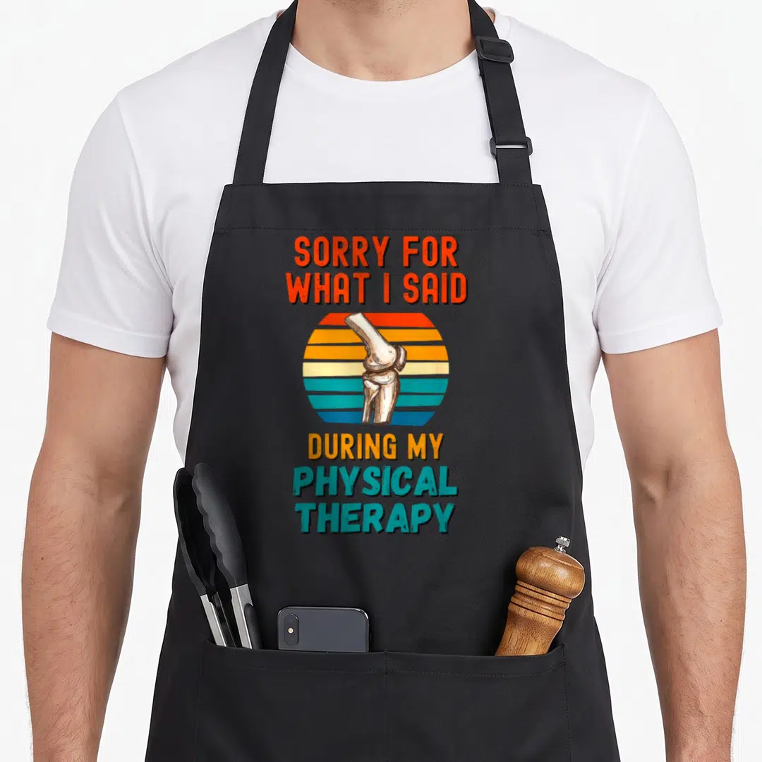 Surgery my therapy apron - Retro knee joint over striped sun with text sorry for what I said during physical therapy — shown on a black cotton canvas apron against a white background