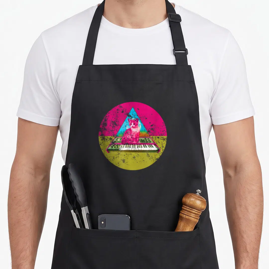 Analog cat apron - Pink cat sitting on synthesizer keys inside a blue triangle and distressed circle — shown on a black cotton canvas apron against a white background