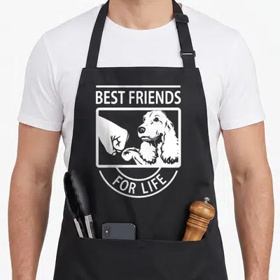 Friend cocker spaniel apron - White line art of dog fist bumping human hand with BEST FRIENDS FOR LIFE text — shown on a black cotton canvas apron against a white background