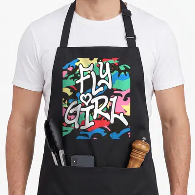 Fly camo apron - Stacked FLY GIRL text with heart on colorful camouflage pattern — shown on a black cotton canvas apron against a white background