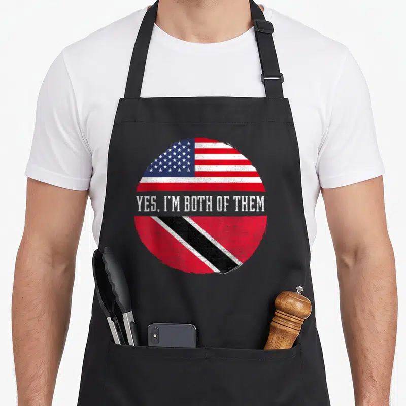 Trinidad american flag apron - Distressed circular design with US and Trinidad flags and text Yes Im Both Of Them — shown on a black cotton canvas apron against a white background