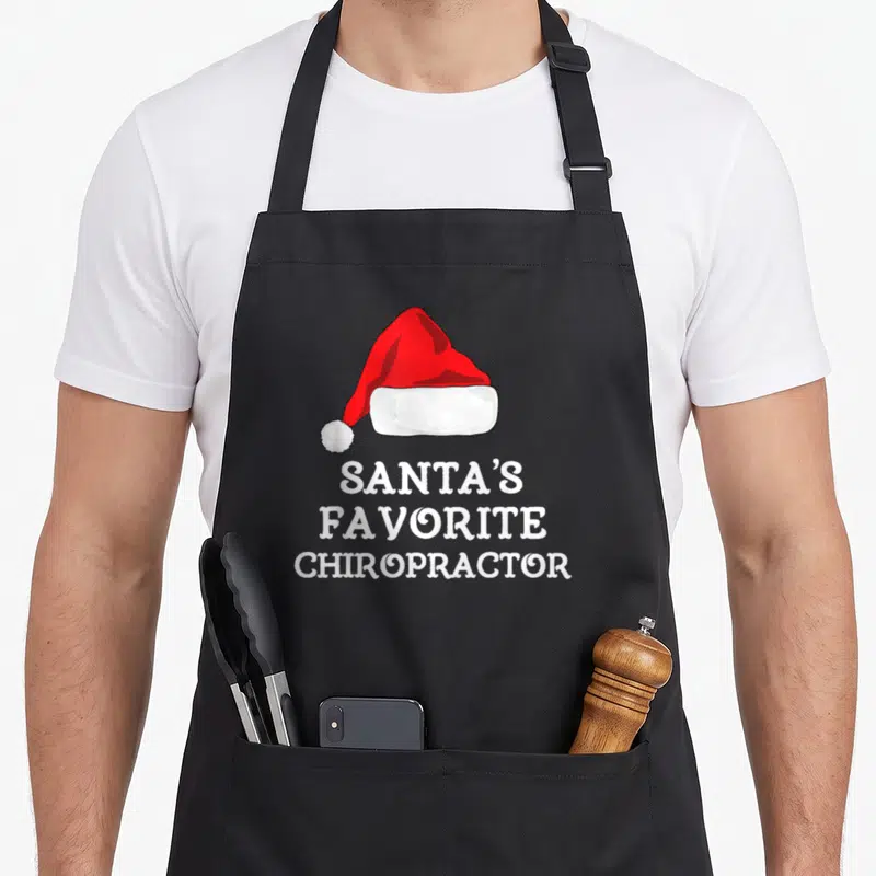 Chiropractor christmas apron - Red Santa hat above white text reading Santa's Favorite Chiropractor — shown on a black cotton canvas apron against a white background