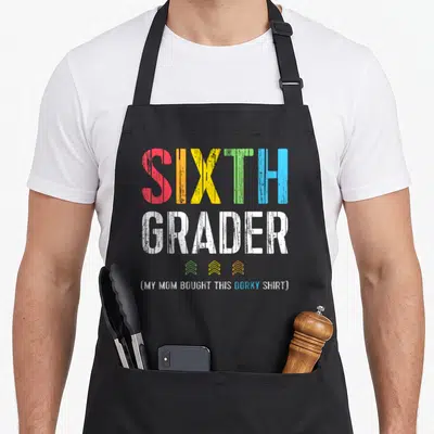 6th grade apron - Stacked colorful text reading SIXTH GRADER with three small chevrons and parenthetical joke below — shown on a black cotton canvas apron against a white background