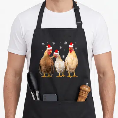 Pajamas family christmas aprons - Three chickens in Santa hats with white snowflakes and dots — shown on a black cotton canvas apron against a white background