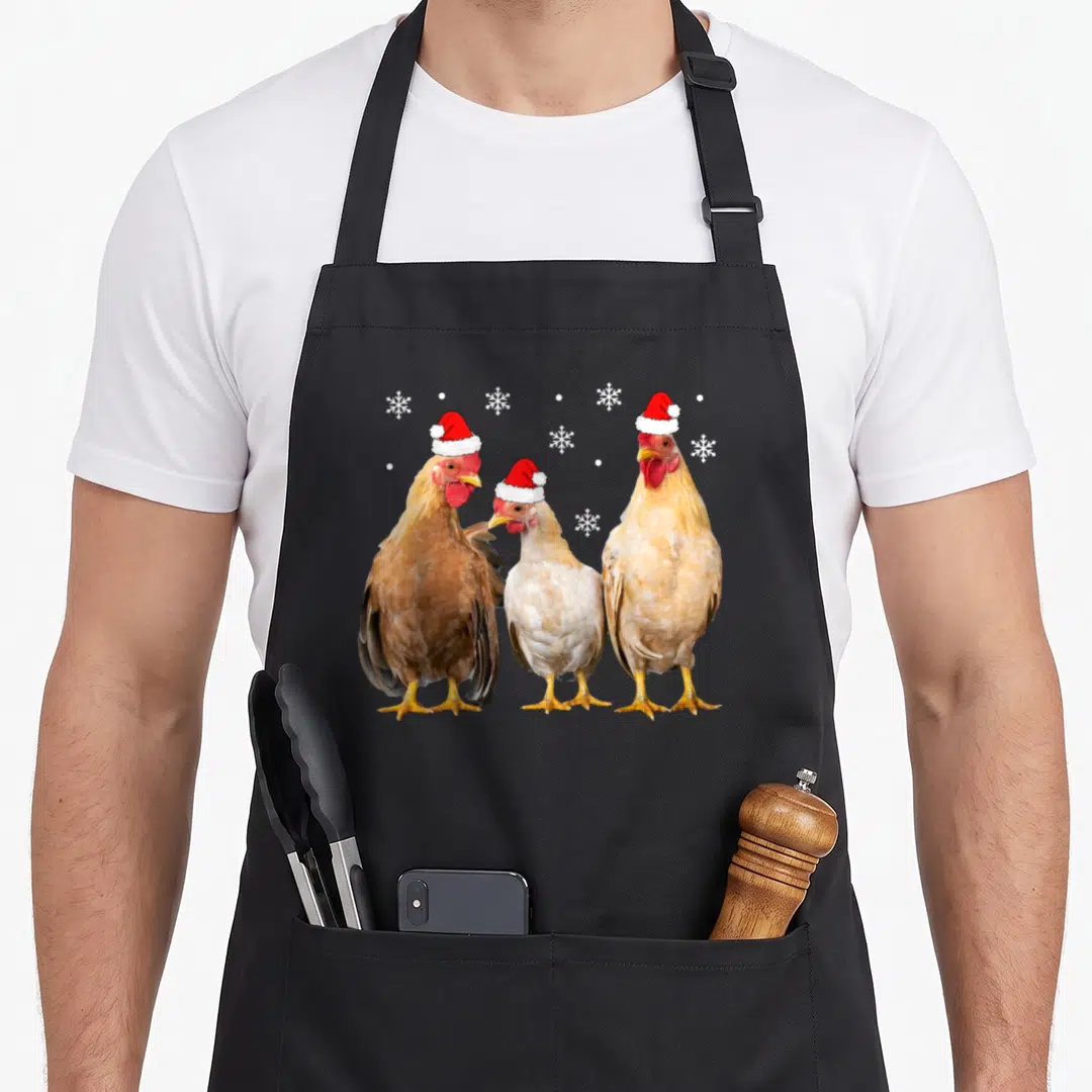 Pajamas family christmas aprons - Three chickens in Santa hats with white snowflakes and dots — shown on a black cotton canvas apron against a white background