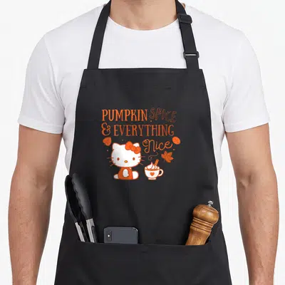 Funny pumpkin spice apron - Hello Kitty sits near a coffee cup under orange text reading PUMPKIN SPICE & EVERYTHING Nice — shown on a black cotton canvas apron against a white background