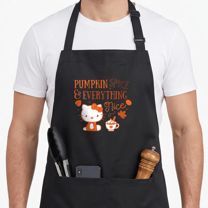 Funny pumpkin spice apron - Hello Kitty sits near a coffee cup under orange text reading PUMPKIN SPICE & EVERYTHING Nice — shown on a black cotton canvas apron against a white background