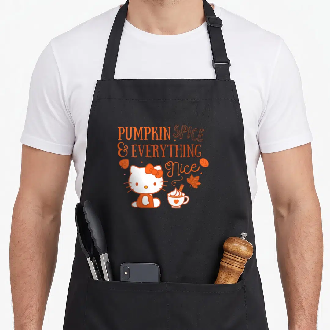 Funny pumpkin spice apron - Hello Kitty sits near a coffee cup under orange text reading PUMPKIN SPICE & EVERYTHING Nice — shown on a black cotton canvas apron against a white background