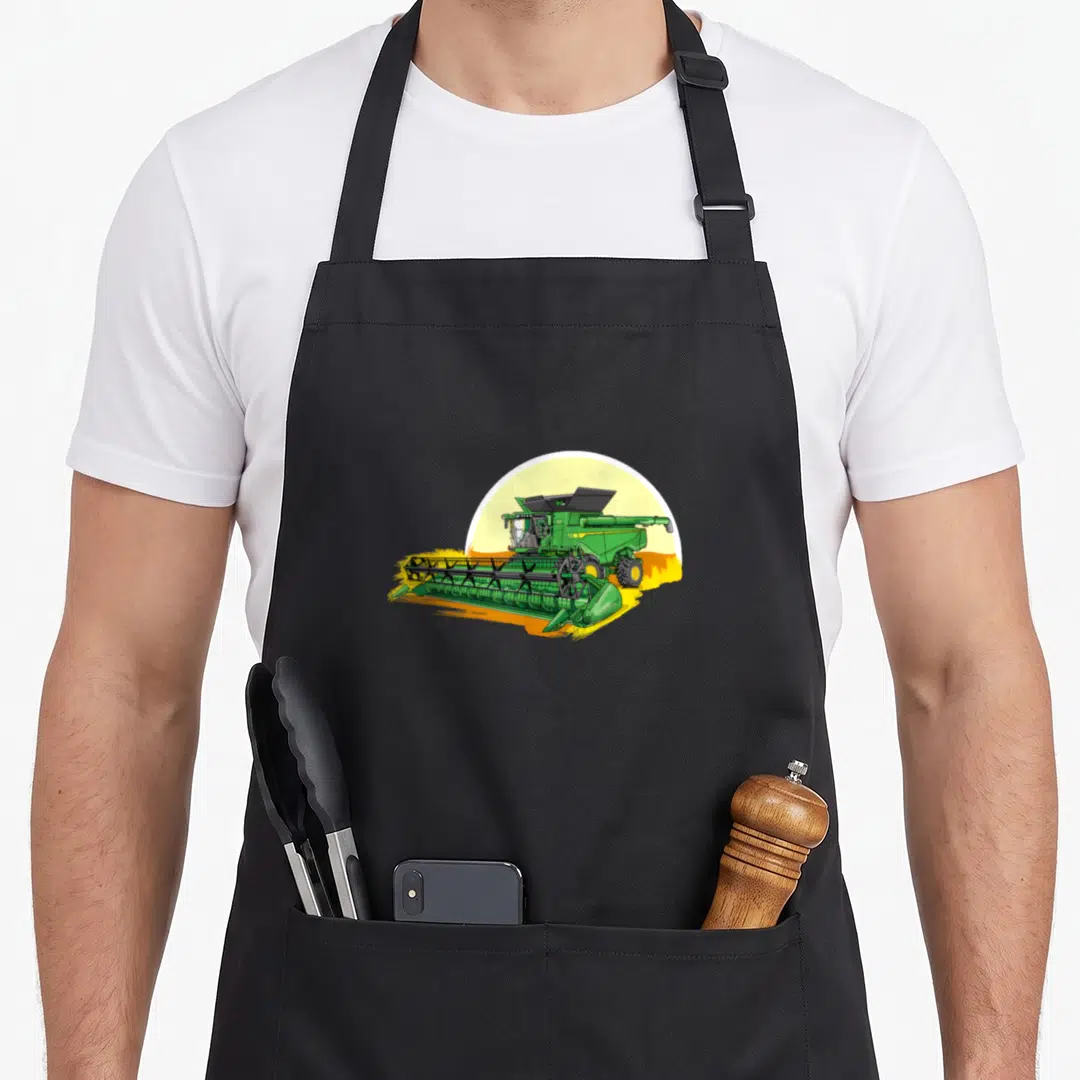 Harvester combine apron - Green combine harvester cartoon centered before yellow semi-circle sun, no text — shown on a black cotton canvas apron against a white background